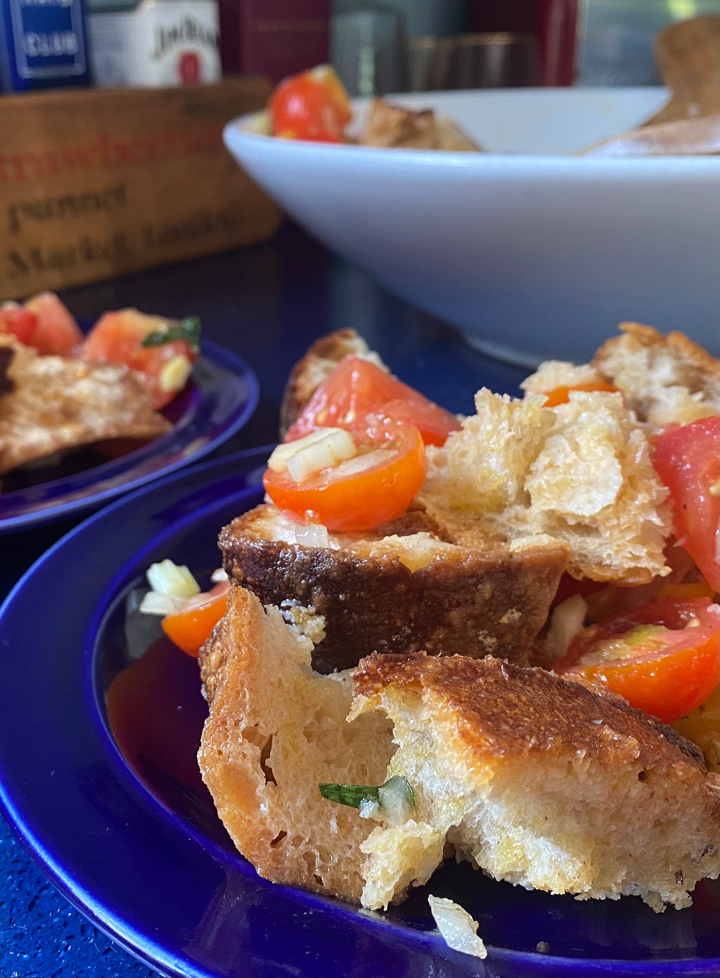 Blue plate serving bread and tomato salad. A larger white serving bowl is behind.