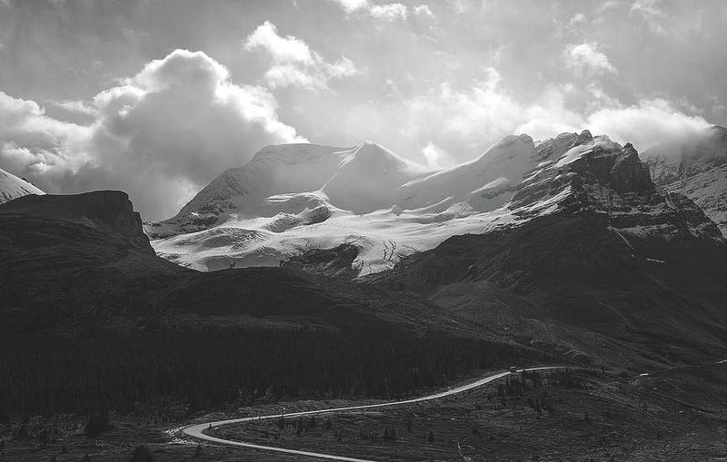 Black and white image of Mount Athabasca with the Columbia Icefield Road leading into snow-covered peaks under a moody sky.