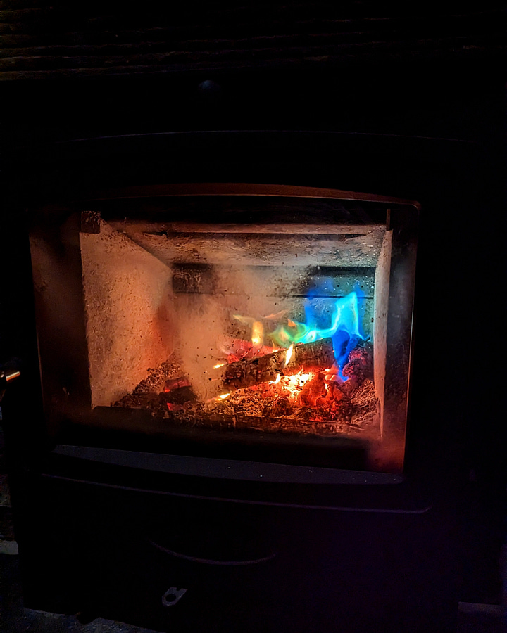 Image one is a photo of Moniack Mhor main house, a dark silhouette against the light of a full moon. The second is a photo of the living room fire, glowing multi-coloured from salt-coated pine cones.