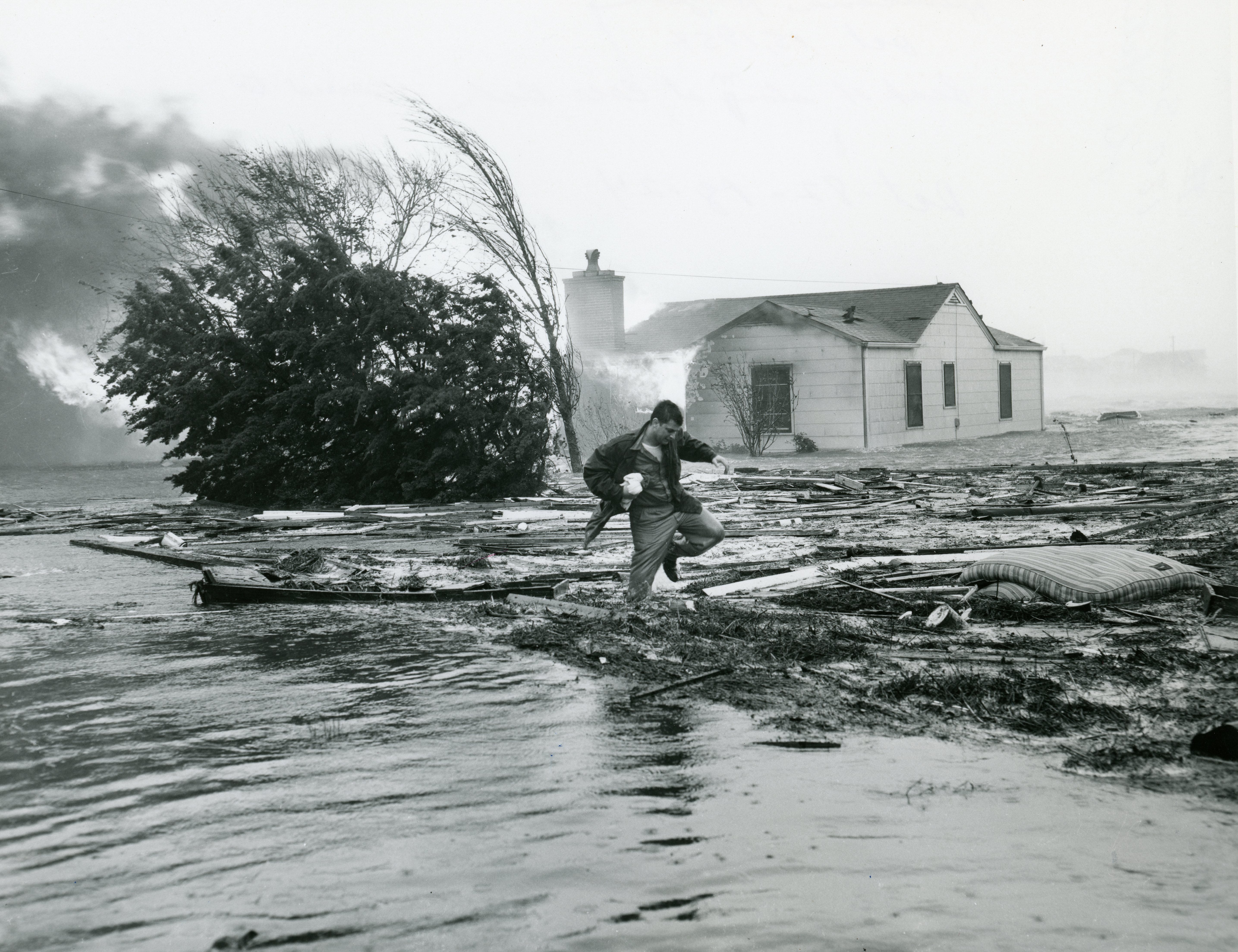Man walking through flood water in front of a burning house during a hurricane. Man walking through flood water in front of a burning house during a hurricane.