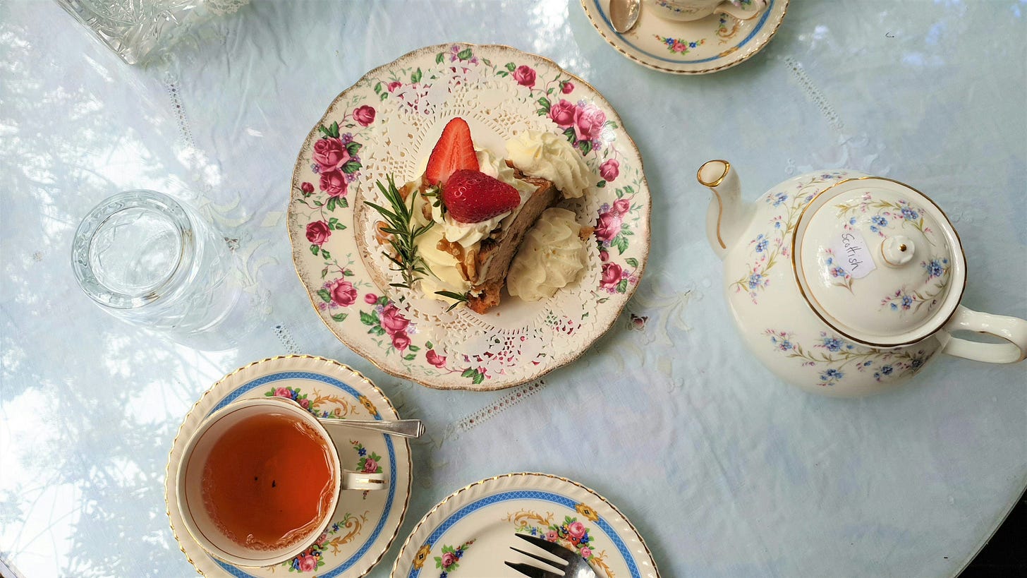 Strawberry cake and black tea are on a table. The china service is a beautifully old fashioned set of flowers.