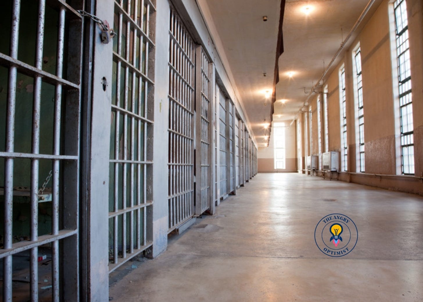 An empty prison corridor with bars along one side and windows along the other An empty prison corridor with bars along one side and windows along the other