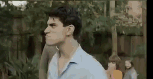 a man in a blue shirt is standing in a park with trees in the background