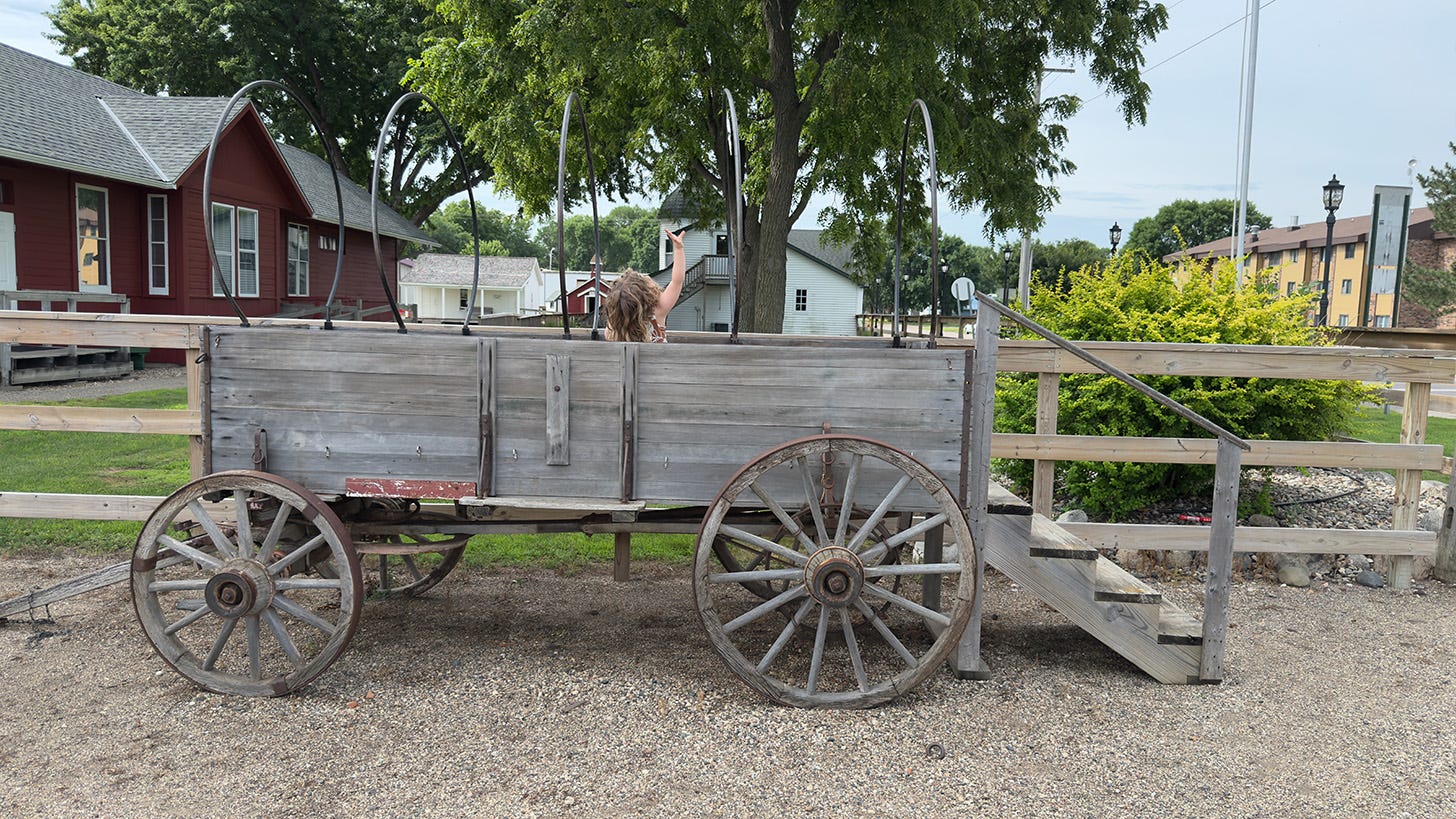 A small kid reaching up to the top of a wagon. The cover has been removed for a photo opportunity.