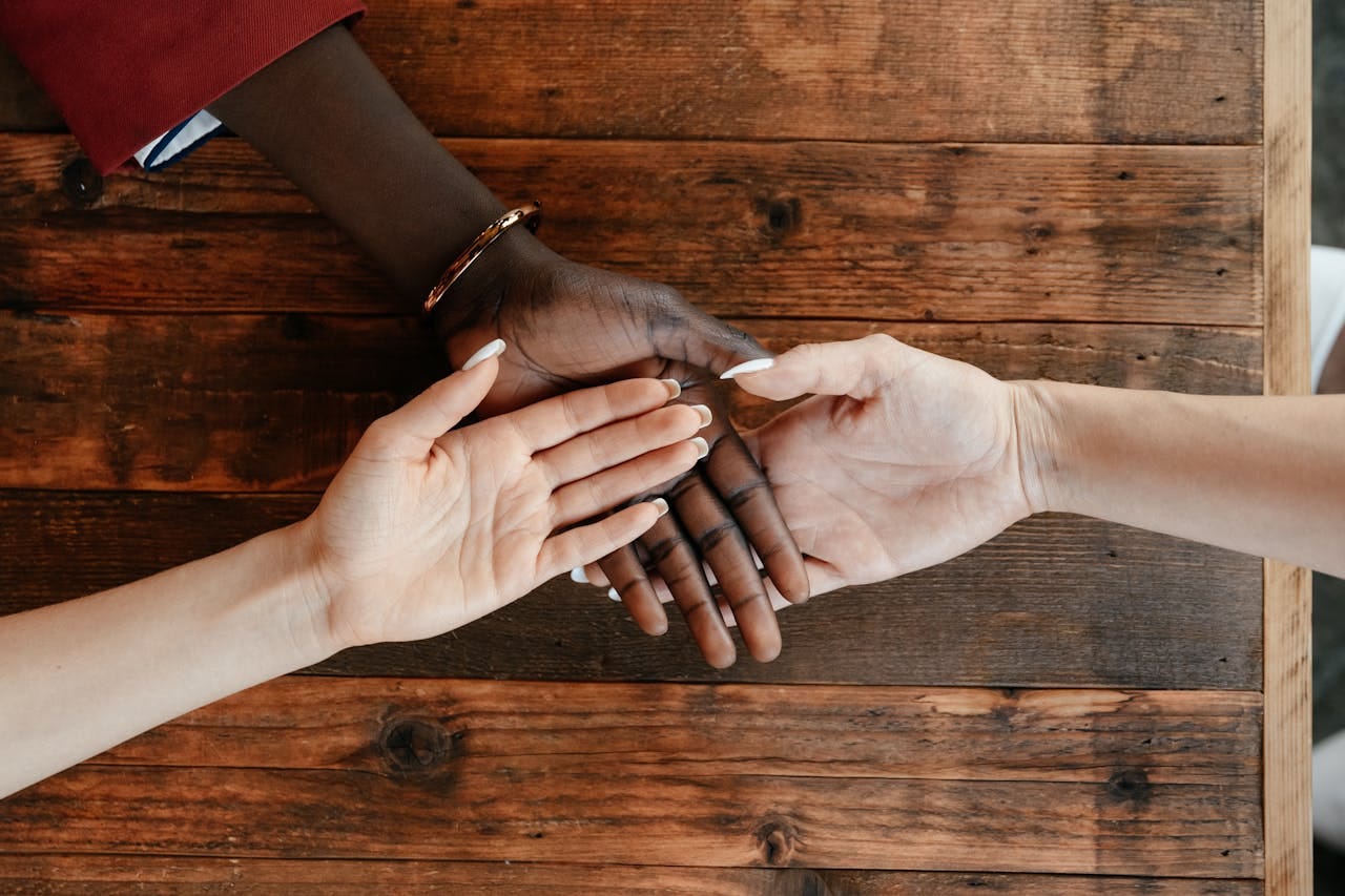 Three women are stacking their hands on a wooden table with their palms facing up.