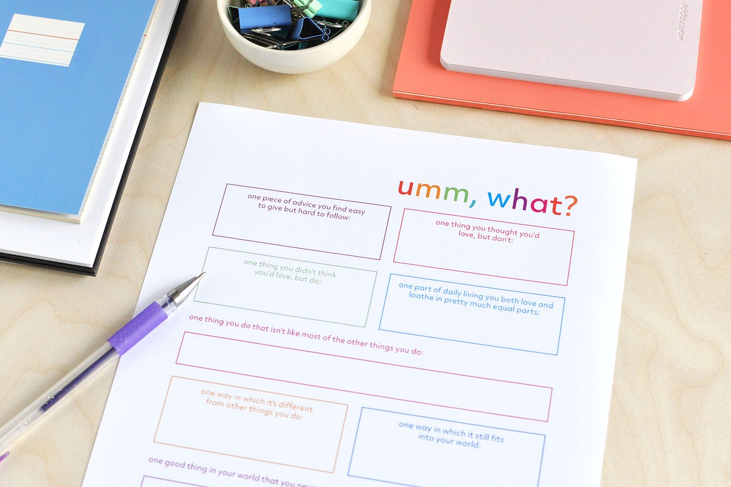 A colourful journal page titled Umm, What, filled with writing prompts for exploring unexpected things and experiences. Shown with a purple pen and colourful notebooks.