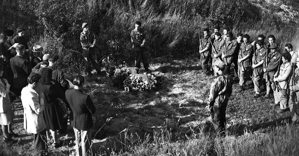 Cerimonia commemorativa a Pian del Lot, Torino. Partigiani armati e civili in lutto attorno a una corona di fiori sul luogo dell'eccidio nazista del 2 aprile 1944.