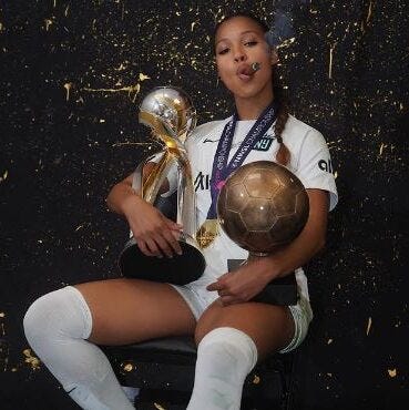 Gotham FC forward Midge Purce celebrates an NWSL title while holding two trophies and smoking a cigar.