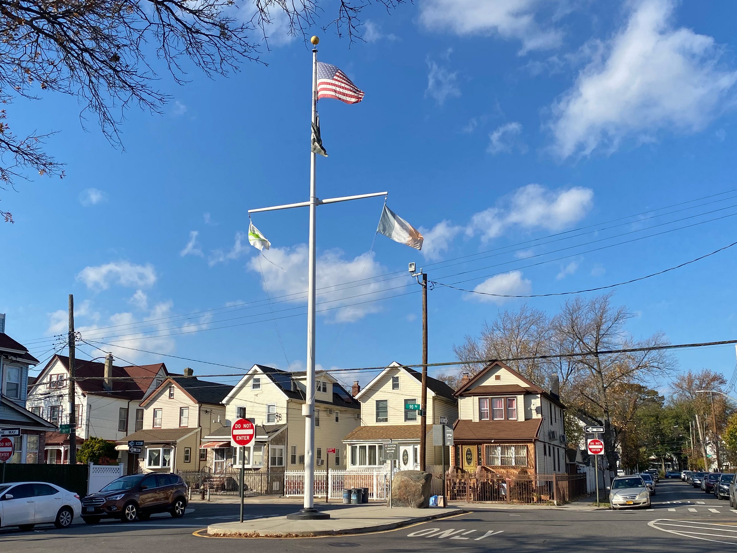 Image is a photograph of Whiting Square looking north at the flagpole and rock with parks department sign. 
