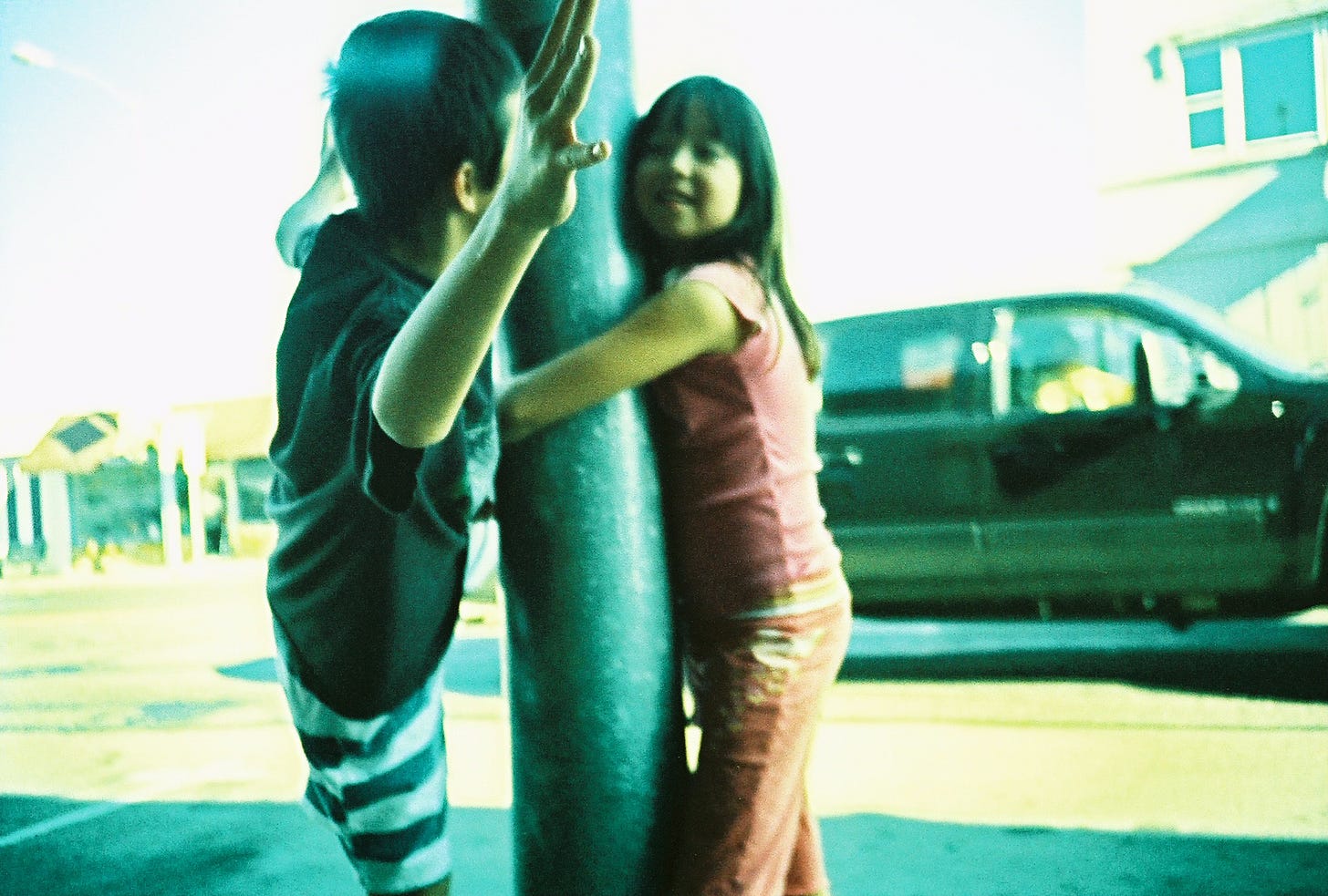 Two kids play at a metal light pole, one surprising the other.
