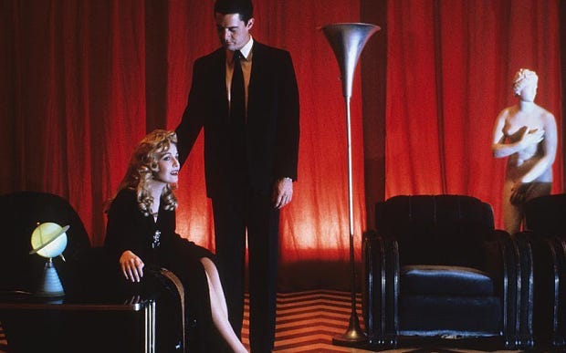 Sheryl Lee sitting in a weird red room; she looks traumatized. Kyle Mclachlan in a suit is reaching down to touch her shoulder as if comforting her. Sheryl Lee sitting in a weird red room; she looks traumatized. Kyle Mclachlan in a suit is reaching down to touch her shoulder as if comforting her.