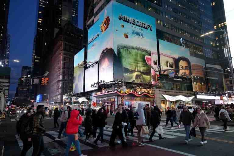 A large crowd of people walking in Times Square under advertising for A Minecraft Movie.