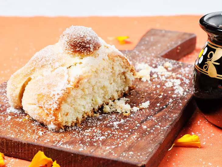 A piece of traditional pan de muerto on a wood cutting board