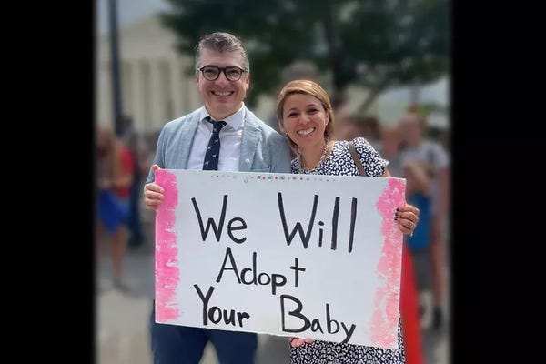 Neydy Casillas and Sebastián Schuff hold a sign that says "We Will Adopt Your Baby"