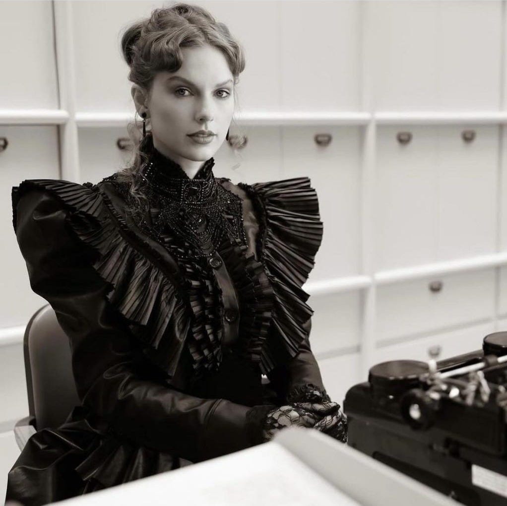 Taylor Swift in Regency costume, sitting opposite her typewriter