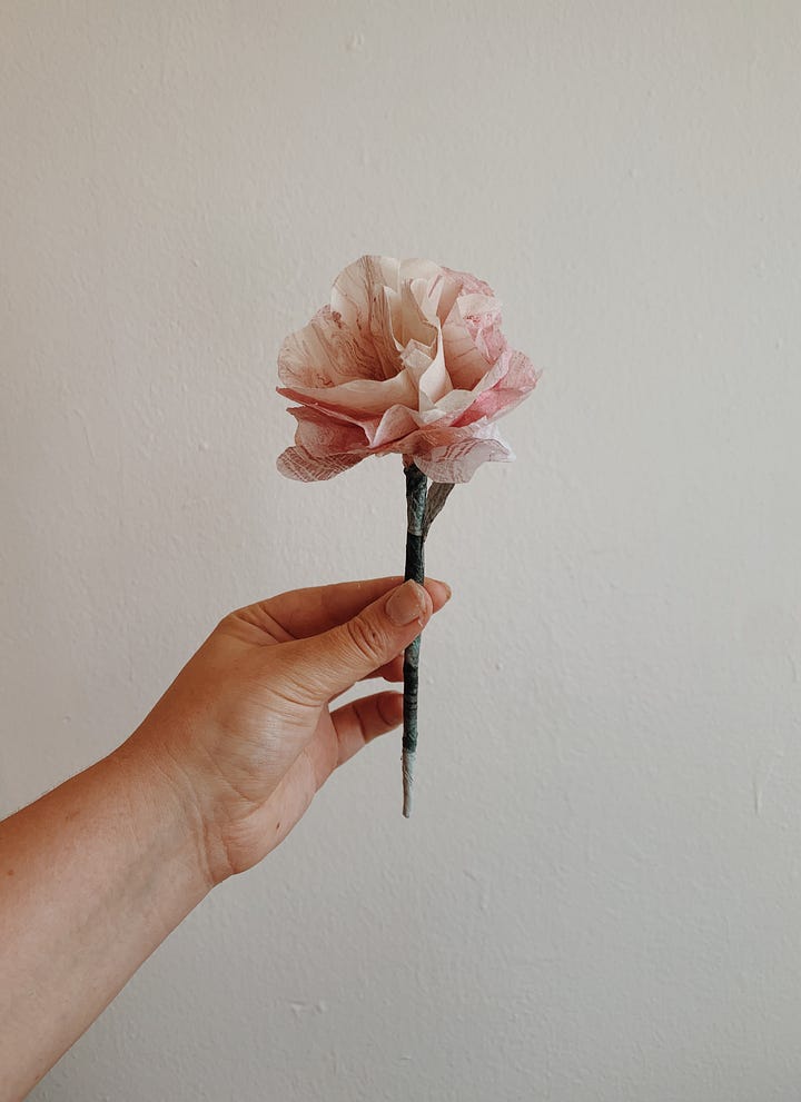 pink paper shaped into a rose on the left, large scale marbled print on the right. the background is dark green, the foreground is white and black marbled paper contrasted against a wall of ivy