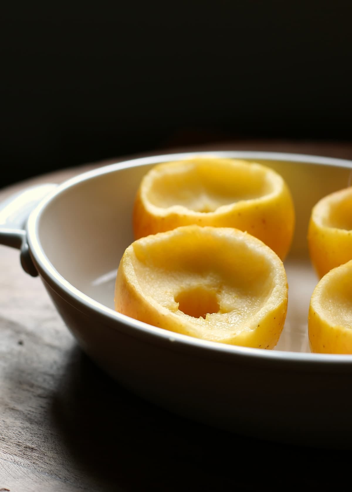 a white baking dish with baked apples in it.