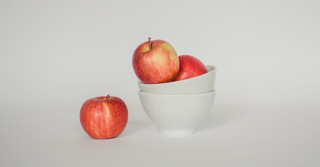 a white bowl filled with red apples on top of a white table