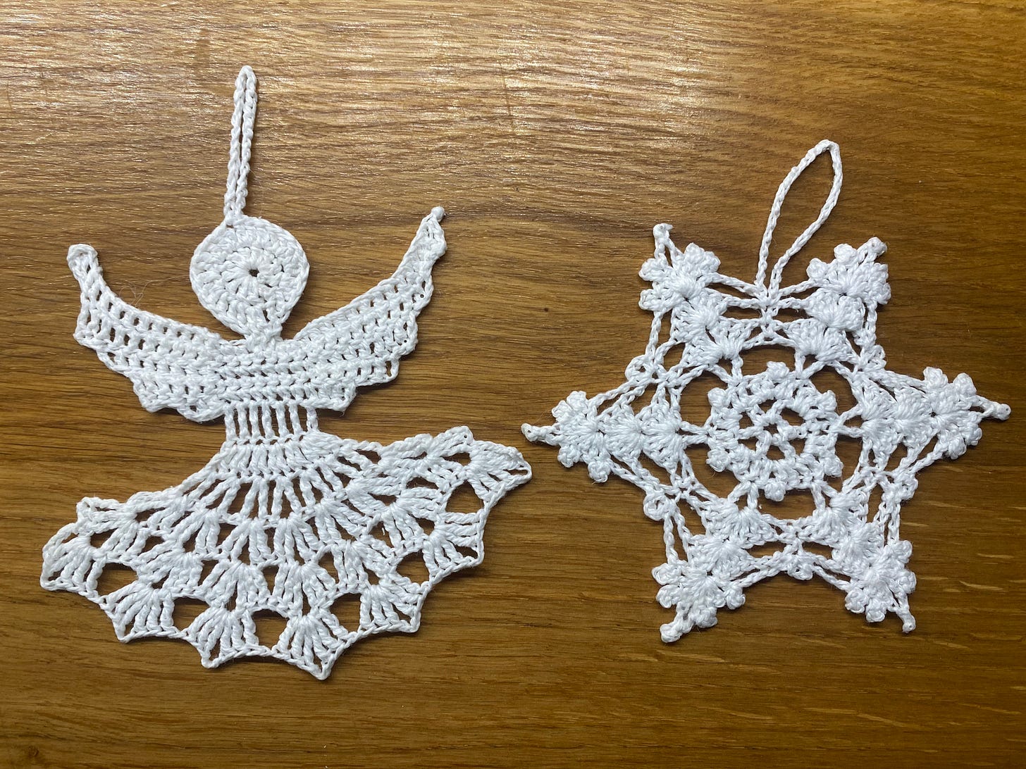Handmade white christmas tree ornaments of an angel and a snowflake against a wooden table.