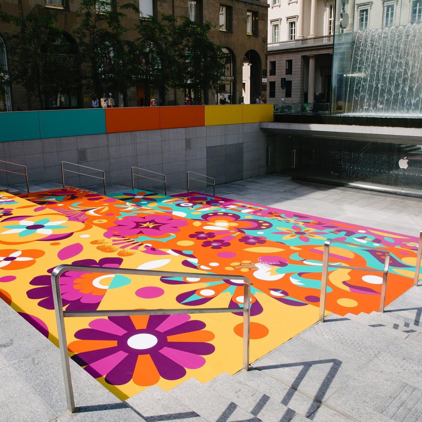 A large, colorful mural covers the amphitheater stairs at Apple Piazza Liberty. A large, colorful mural covers the amphitheater stairs at Apple Piazza Liberty.
