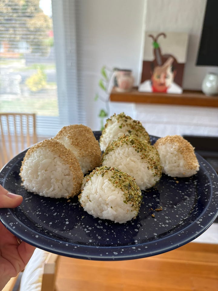 A plate of onigiri on a blue and white speckled serving plate, held up, with a dining table and fireplace in the background. A close up of an onigiri with a bite missing, showing the tuna filling.