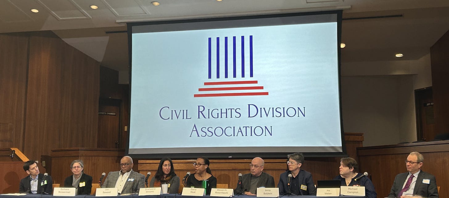 Alt text: A panel of 9 speakers seated at a table below a projected image and name "Civil Rights Division Association"