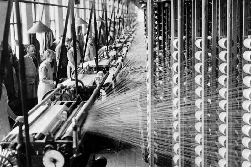 A 1935 factory with cones of cotton thread beamed from a high stack to be warped onto looms.
