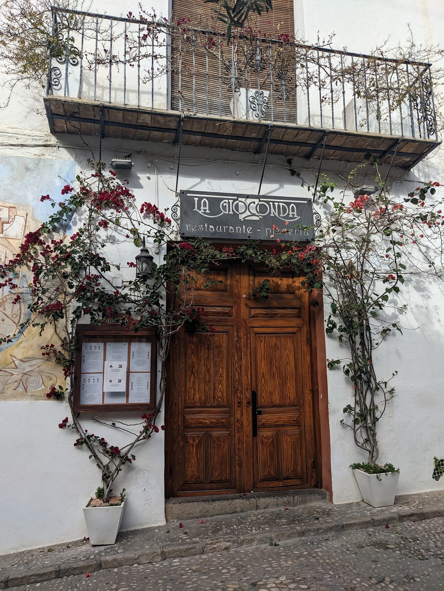 a doorway with a sign over it that says "La Giocanda." It's on a whitewashed building and surrounded by bougainvillea