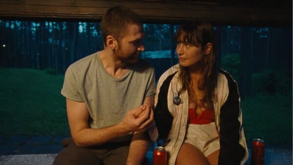 A man in a gray T-shirt sits next to a woman in a red shirt and white shorts. 