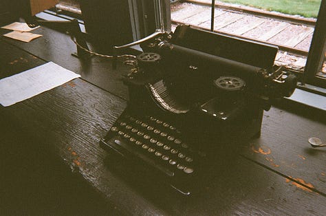 Red train engine with caboose. | An old typewriter used to relay messages to passing trains. | A white and yellow schoolhouse with an American flag.