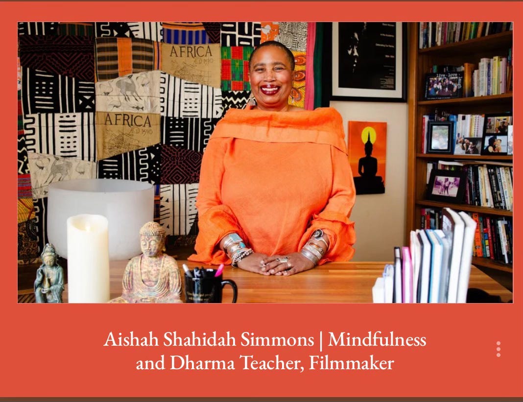 Aishah Shahidah Simmons smiles warmly, wearing an orange off-shoulder linen top and silver jewelry, seated at a wooden desk with Buddha statues, a pillar candle, and a crystal singing bowl. A colorful patchwork quilt featuring African textiles fills the wall behind her, alongside a bookshelf. Text below reads: "Aishah Shahidah Simmons | Mindfulness and Dharma Teacher, Filmmaker." Aishah Shahidah Simmons smiles warmly, wearing an orange off-shoulder linen top and silver jewelry, seated at a wooden desk with Buddha statues, a pillar candle, and a crystal singing bowl. A colorful patchwork quilt featuring African textiles fills the wall behind her, alongside a bookshelf. Text below reads: "Aishah Shahidah Simmons | Mindfulness and Dharma Teacher, Filmmaker."