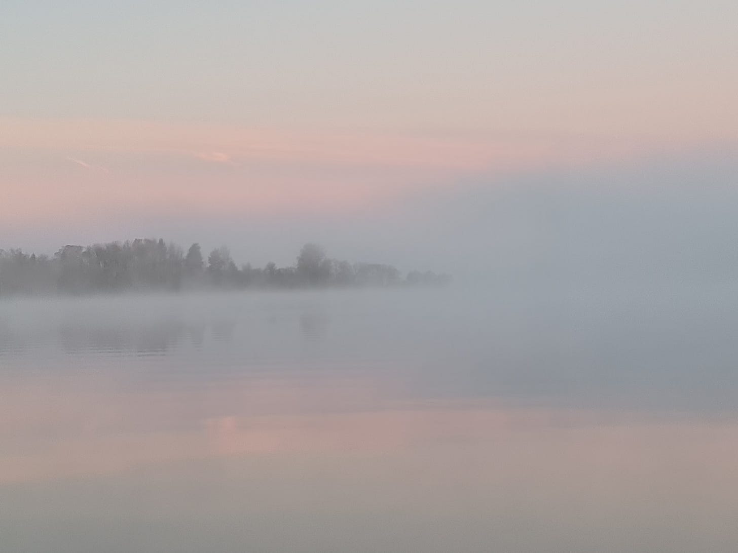 Sjörök stiger upp från havet en kall morgon och skymmer den andra stranden. Morgonrodnadnen spelgar sig i vattnet.