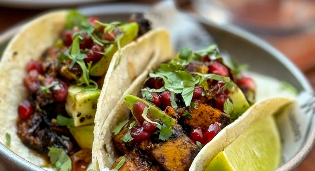 Two tacos on a silver plate with a wedge of lime next to them