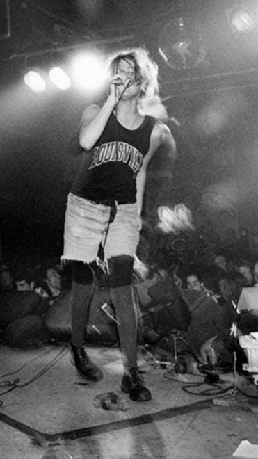 Mia Zapata fotografata da Charles Peterson a Seattle nel 1993.
Mia è in piedi sul palco e canta con gli occhi chiusi dando le spalle al pubblico. Mia Zapata fotografata da Charles Peterson a Seattle nel 1993.
Mia è in piedi sul palco e canta con gli occhi chiusi dando le spalle al pubblico.