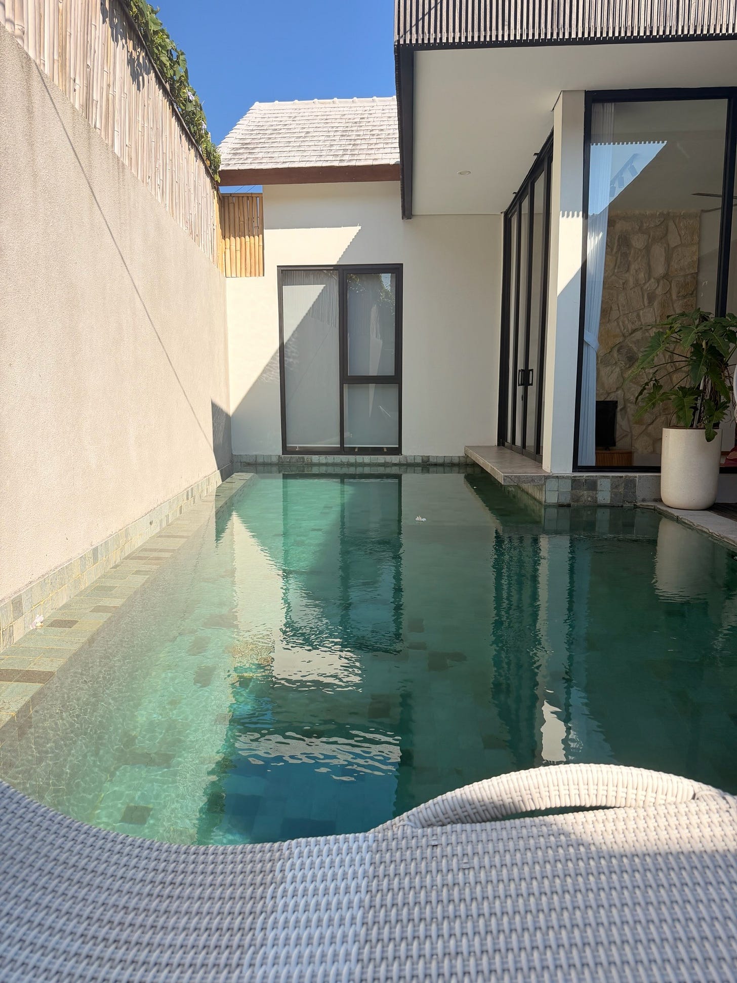 Morning view of a Bali villa garden with a pool and tropical greenery in morning light.