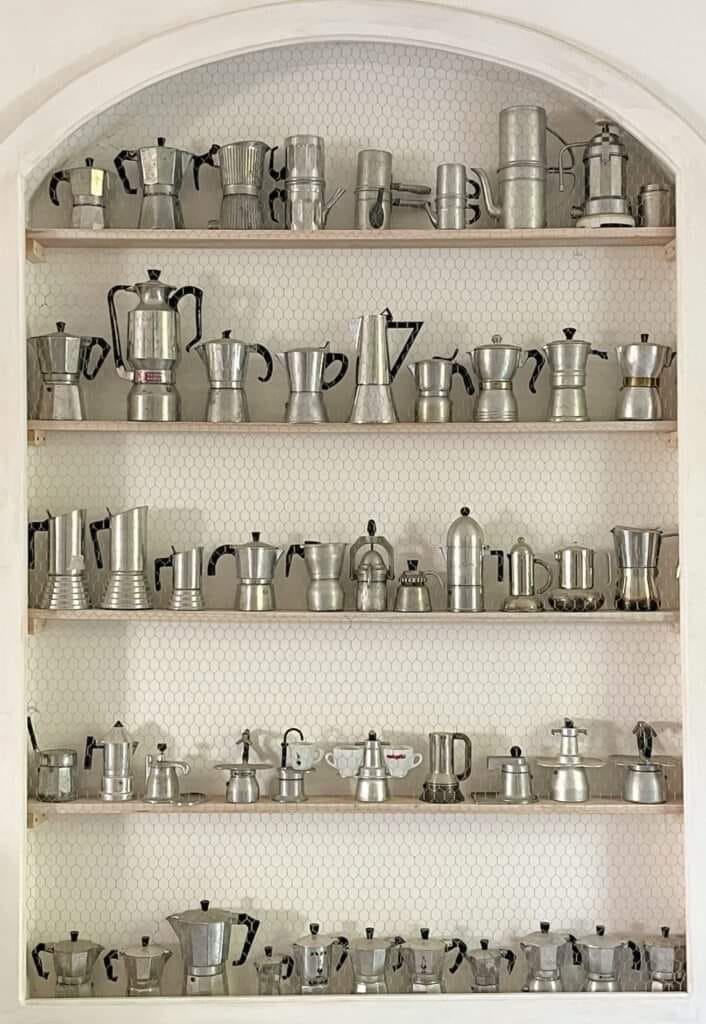 This may contain: a shelf filled with lots of metal cups and saucepans on top of wooden shelves