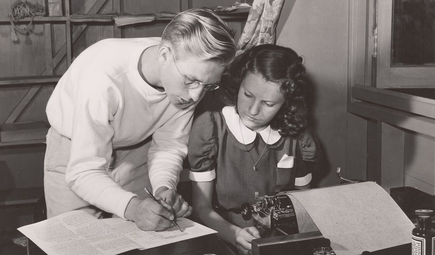 black and white photograph showing an editor standing next to a woman at a typewriter, marking a page while she looks on black and white photograph showing an editor standing next to a woman at a typewriter, marking a page while she looks on