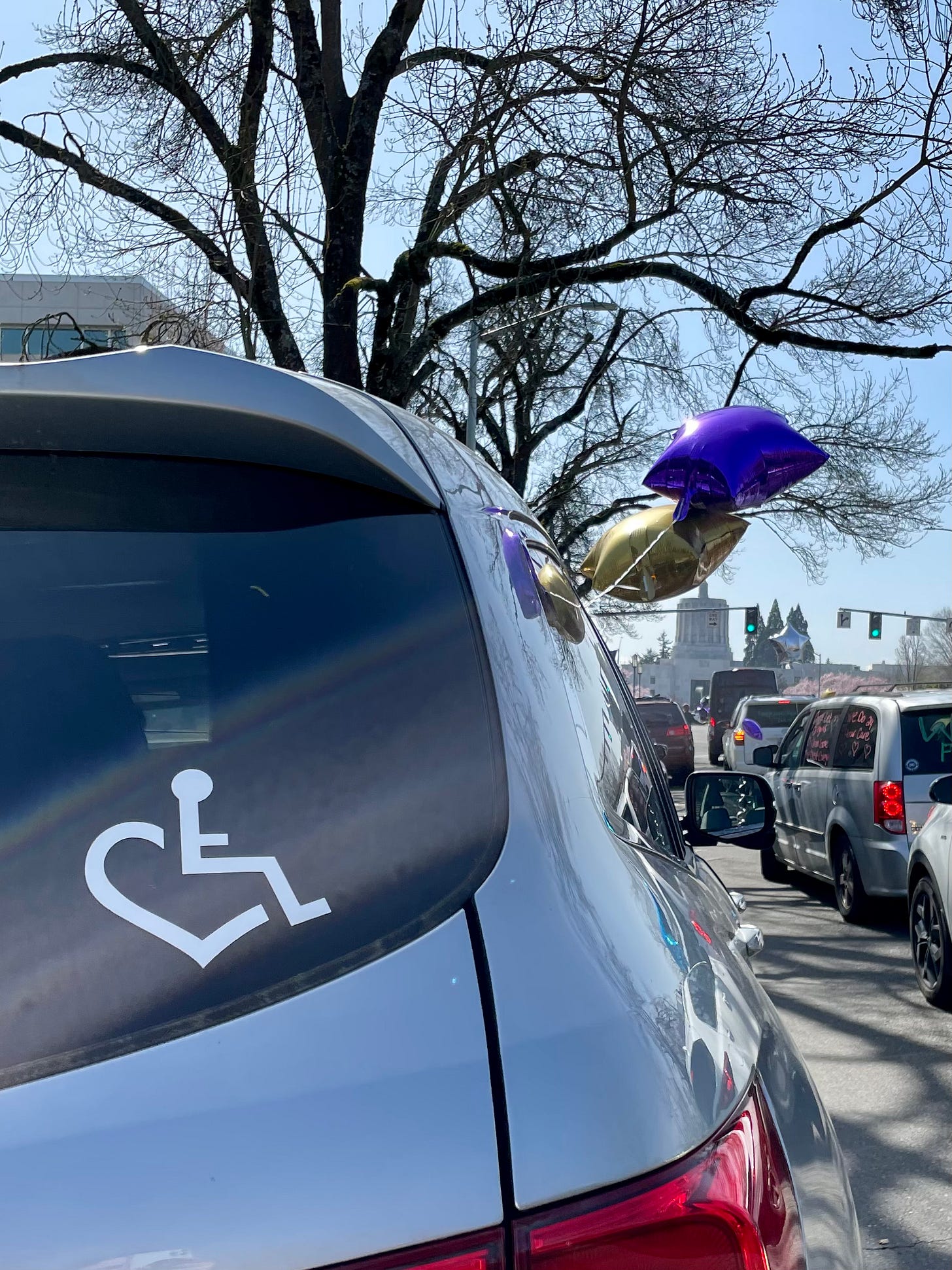 A van with a universal access symbol heart parks on the street with The Capitol building in the distance.