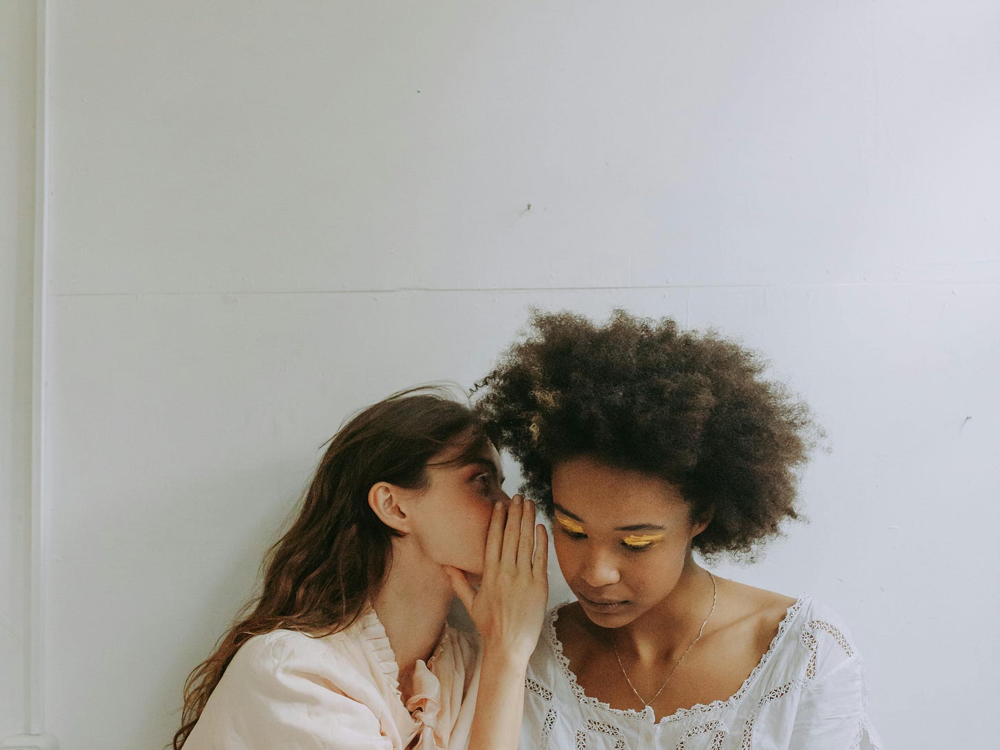 Free Two women seated indoors, whispering secrets in a calm and minimalist space. Stock Photo