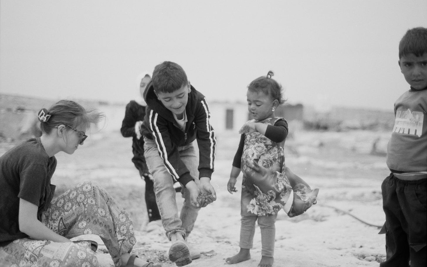 A black and white photo of an adult and three Palestinian children playing outside.