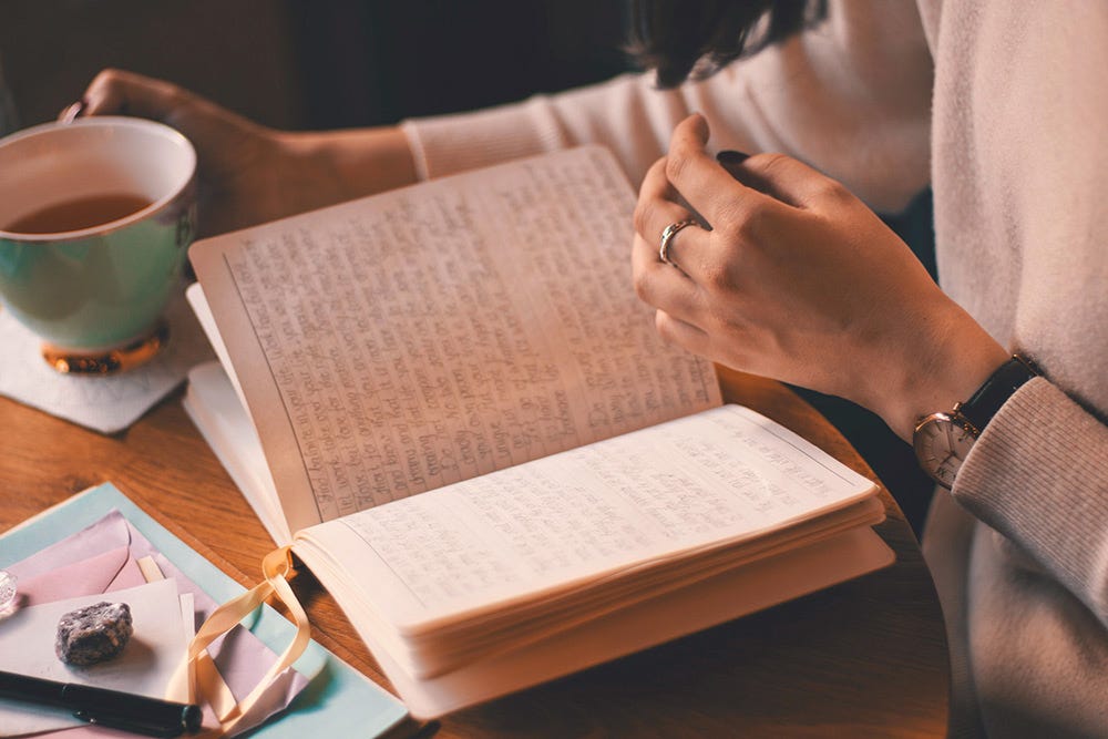 Devant un carnet rempli de notes, une silhouette attrape l'anse d'une tasse de café. Devant un carnet rempli de notes, une silhouette attrape l'anse d'une tasse de café.