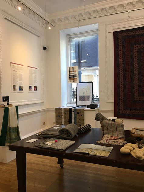 Views of the main exhibition space for Threads of Change at the Nehru Centre showing garments and fabric hanging on the walls with textile artefacts and books on the wooden table.