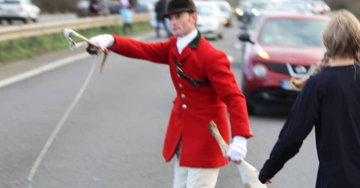 Hunt whipper-in holds a dead hound by the leg on a busy road, with traffic in the background. Hunt whipper-in holds a dead hound by the leg on a busy road, with traffic in the background.