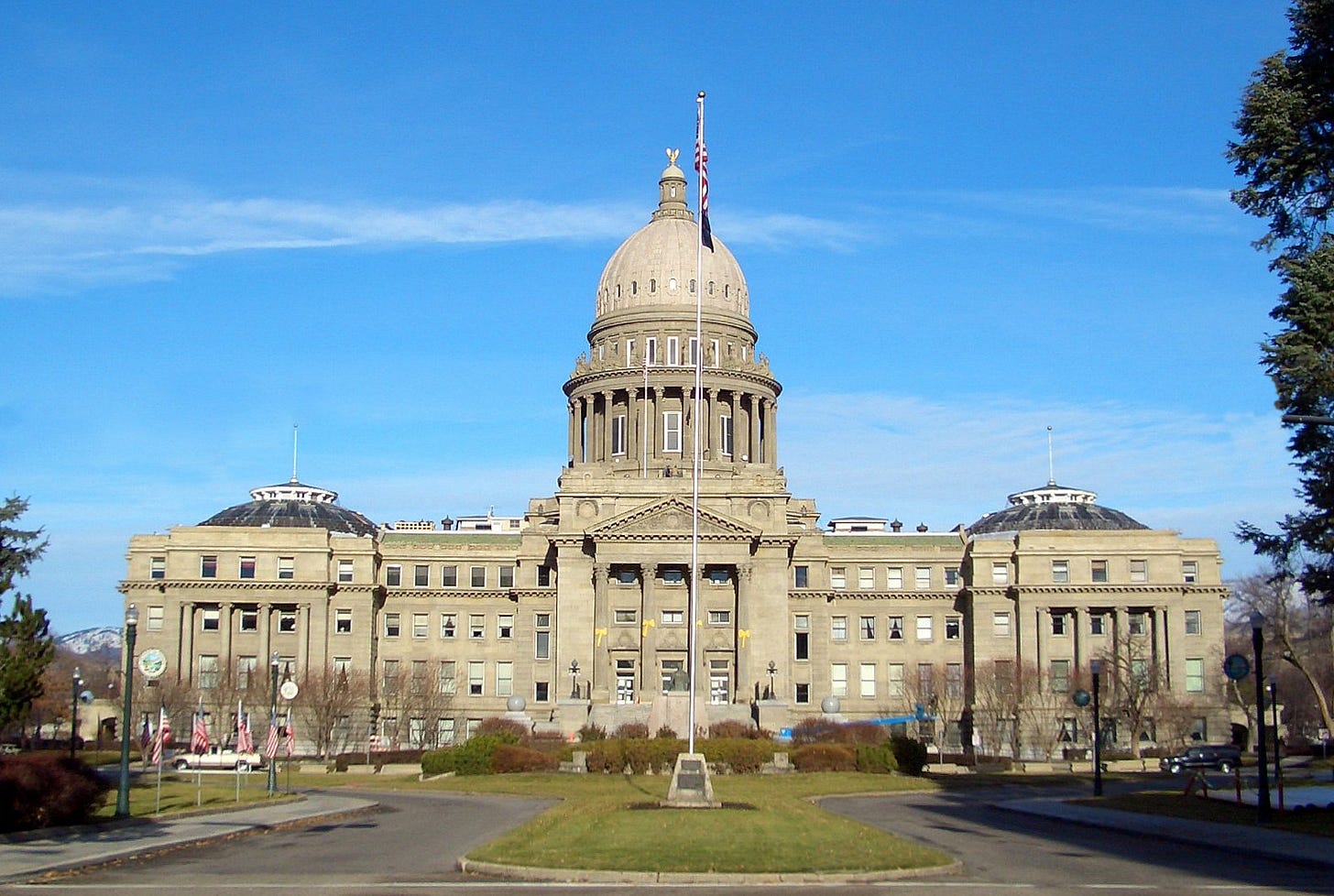 Frontal view of the Idaho State Capitol building in Boise, with a central dome, flagpole, and clear blue sky.