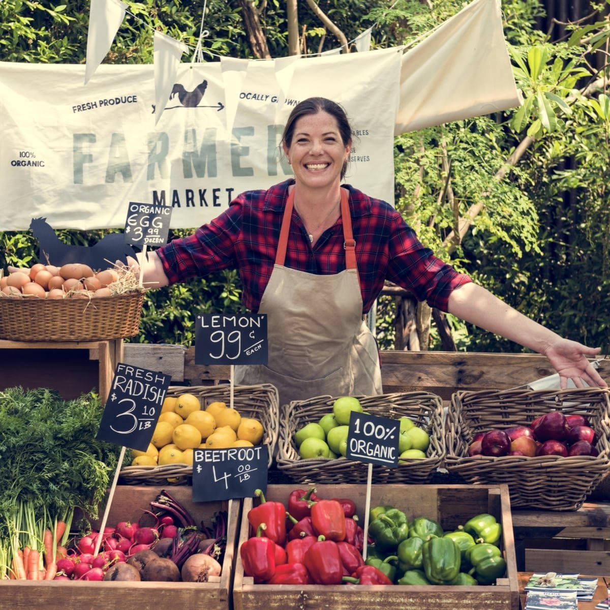 A smiling vendor at a vibrant outdoor farmers market displays fresh produce
