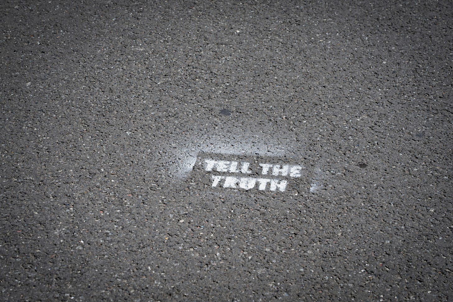 A grey concrete road with white stencilled graffiti that says 'tell the truth' A grey concrete road with white stencilled graffiti that says 'tell the truth'