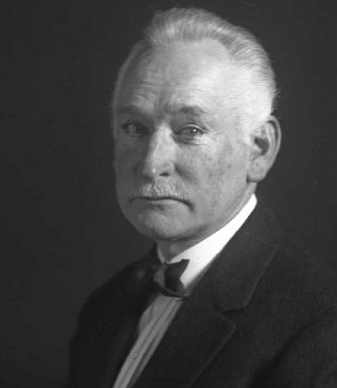 Black-and-white portrait of John Russell Coryell, an older white man with neatly combed back white hair and a trimmed mustache. He wears a dark suit jacket, white shirt, and bow tie, and looks slightly toward the camera with a composed expression against a dark studio background. Black-and-white portrait of John Russell Coryell, an older white man with neatly combed back white hair and a trimmed mustache. He wears a dark suit jacket, white shirt, and bow tie, and looks slightly toward the camera with a composed expression against a dark studio background.