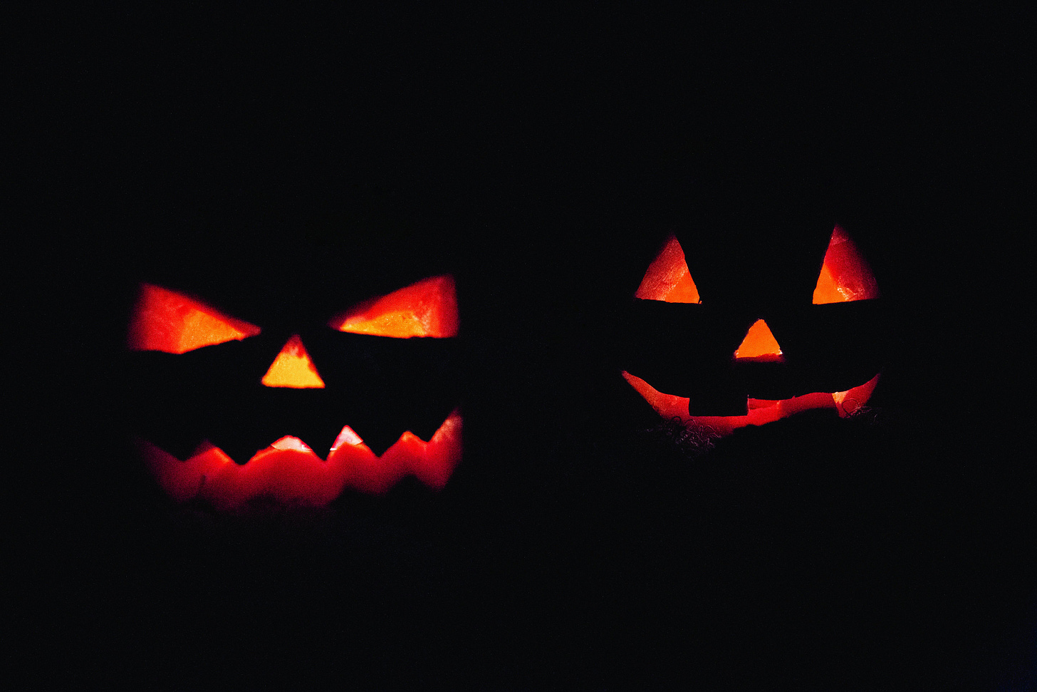 two jack o lanterns with menacing faces in the dark