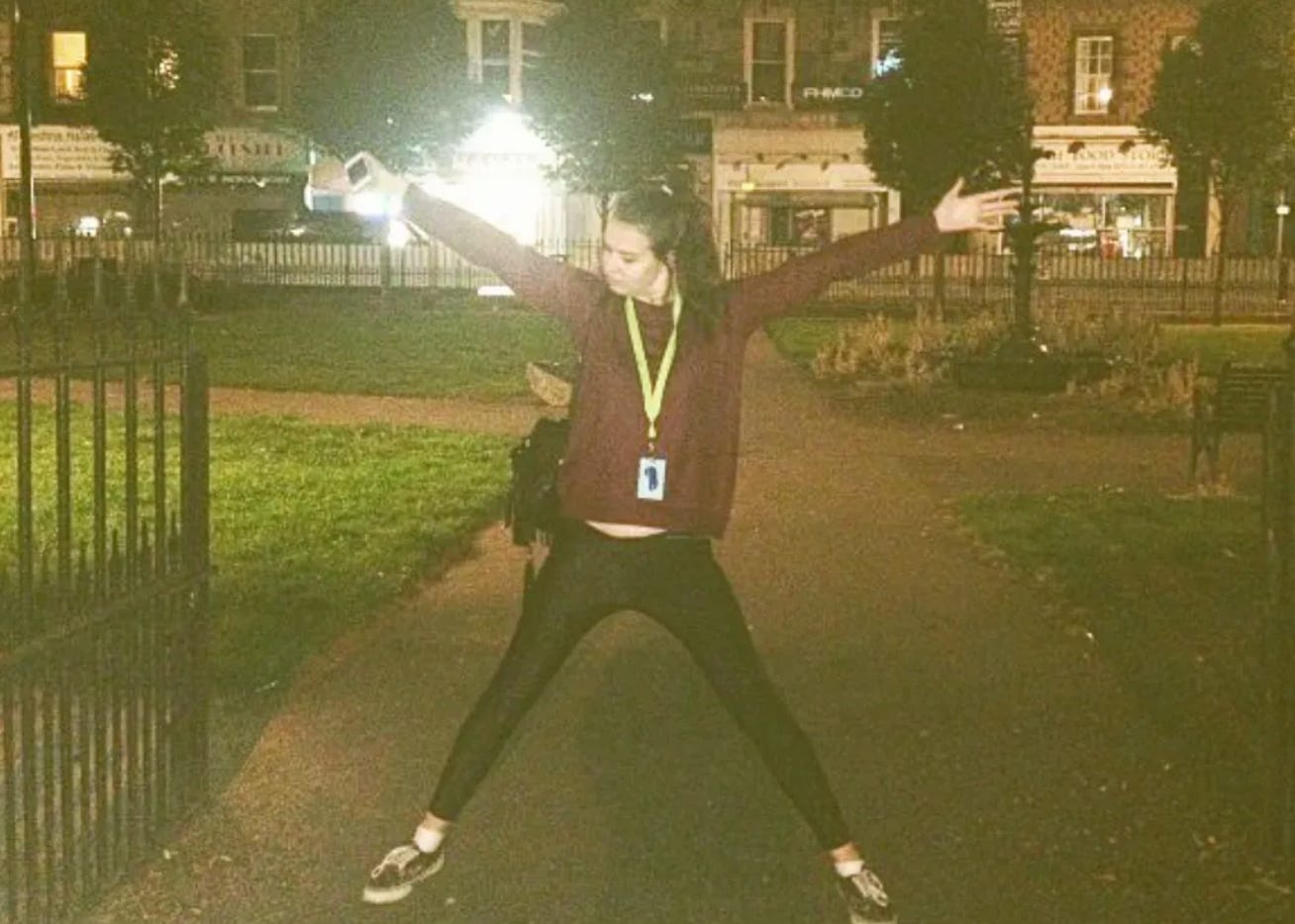 A slightly grainy photo of a young white woman stood in a starjump pose in the open gates of Nicholson Square in Edinburgh. She is wearing shiny black leggings, a purple jumper with a green lanyard and has long dark hair in a ponytail. A slightly grainy photo of a young white woman stood in a starjump pose in the open gates of Nicholson Square in Edinburgh. She is wearing shiny black leggings, a purple jumper with a green lanyard and has long dark hair in a ponytail.