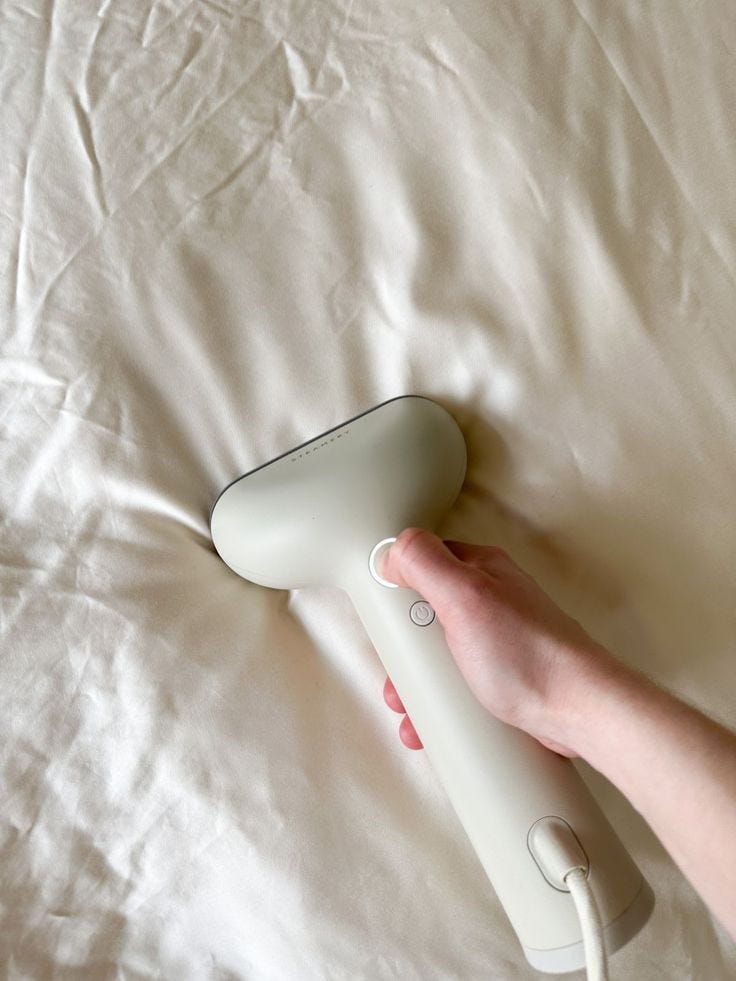 This may contain: a person's hand holding a white hair dryer on top of a bed